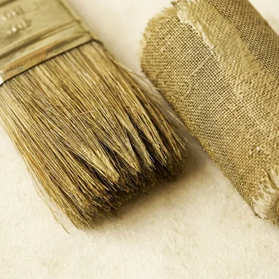 Close-up of clean paintbrush bristles and a roller loaded with a soft aged-brass tone, resting on a bare parchment surface